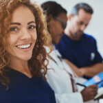 Smiling young female healthcare professional, doctor standing in a hospital corridor with two medical colleagues talking in the background