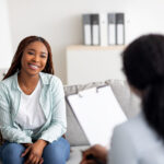 Successful therapy. Young female client having consultation with psychologist, grateful for professional help at clinic. Happy black lady speaking with her psychotherapist, solving emotional problem
