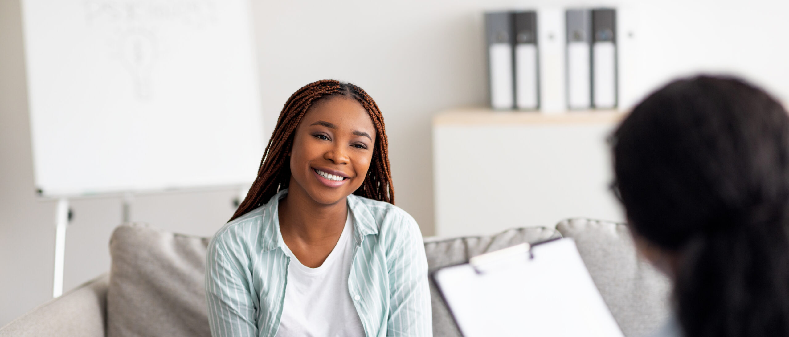 Successful therapy. Young female client having consultation with psychologist, grateful for professional help at clinic. Happy black lady speaking with her psychotherapist, solving emotional problem