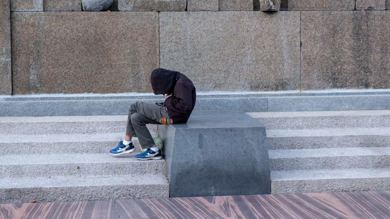 A young lonely boy in the park checking his mobile phone