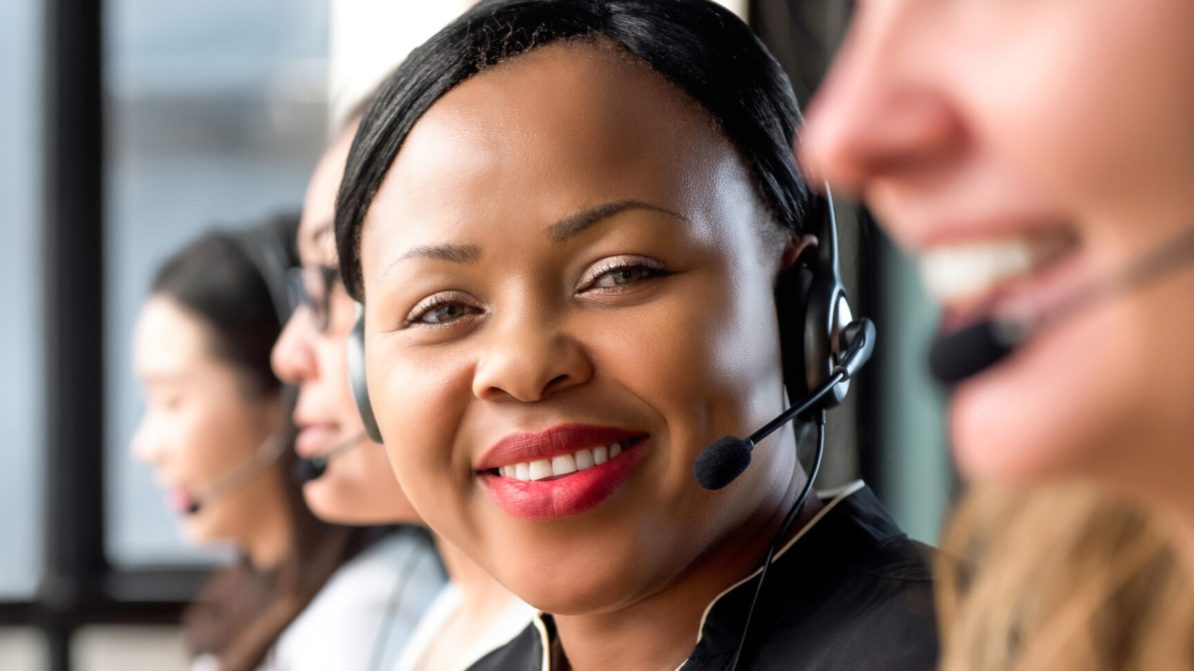 Friendly black woman wearing microphone headset working in call center with international team as telemarketing customer service agents, panoramic banner
