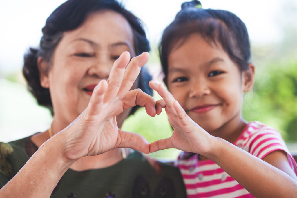 Grandmother and little child girl making heart shape with hands together with love