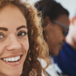 Smiling young female healthcare professional, doctor standing in a hospital corridor with two medical colleagues talking in the background